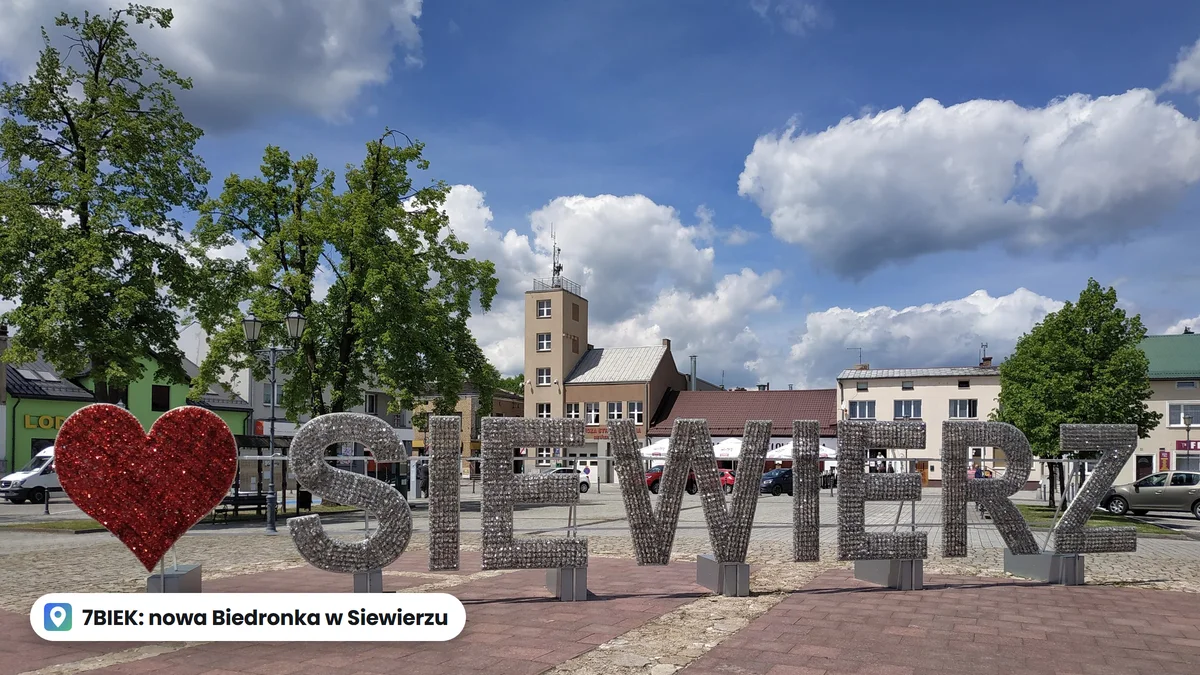 Napis Siewierz i czerwone serce na rynku w Siewierzu, w tle kamienice i wieża straży pożarnej