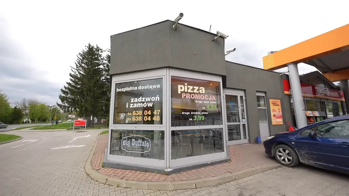 Front lokalu Big Buffalo w Zamościu z napisami o promocji na pizzę i bezpłatnej dostawie, obok stacja benzynowa