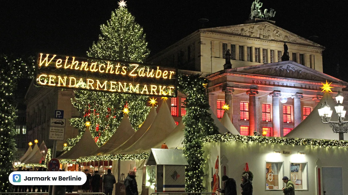 Wejście na jarmark WeihnachtsZauber na Gendarmenmarkt w Berlinie nocą: świetlny napis, choinka, białe namioty i oświetlony gmach Konzerthaus