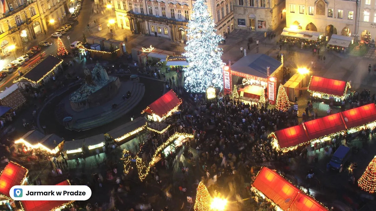 Jarmark bożonarodzeniowy na Rynku Staromiejskim w Pradze z góry: czerwone dachy straganów, choinka i tłum wieczorem