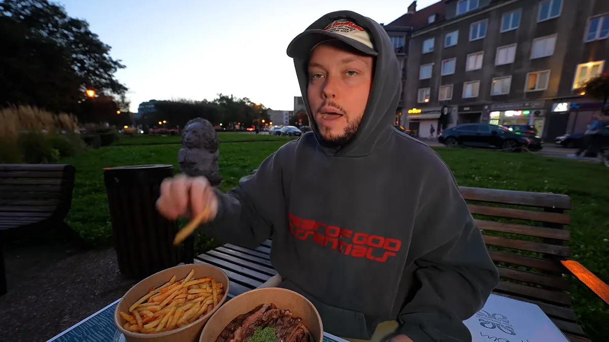 Książulo w kapturze i czapce je frytki na ławce w parku