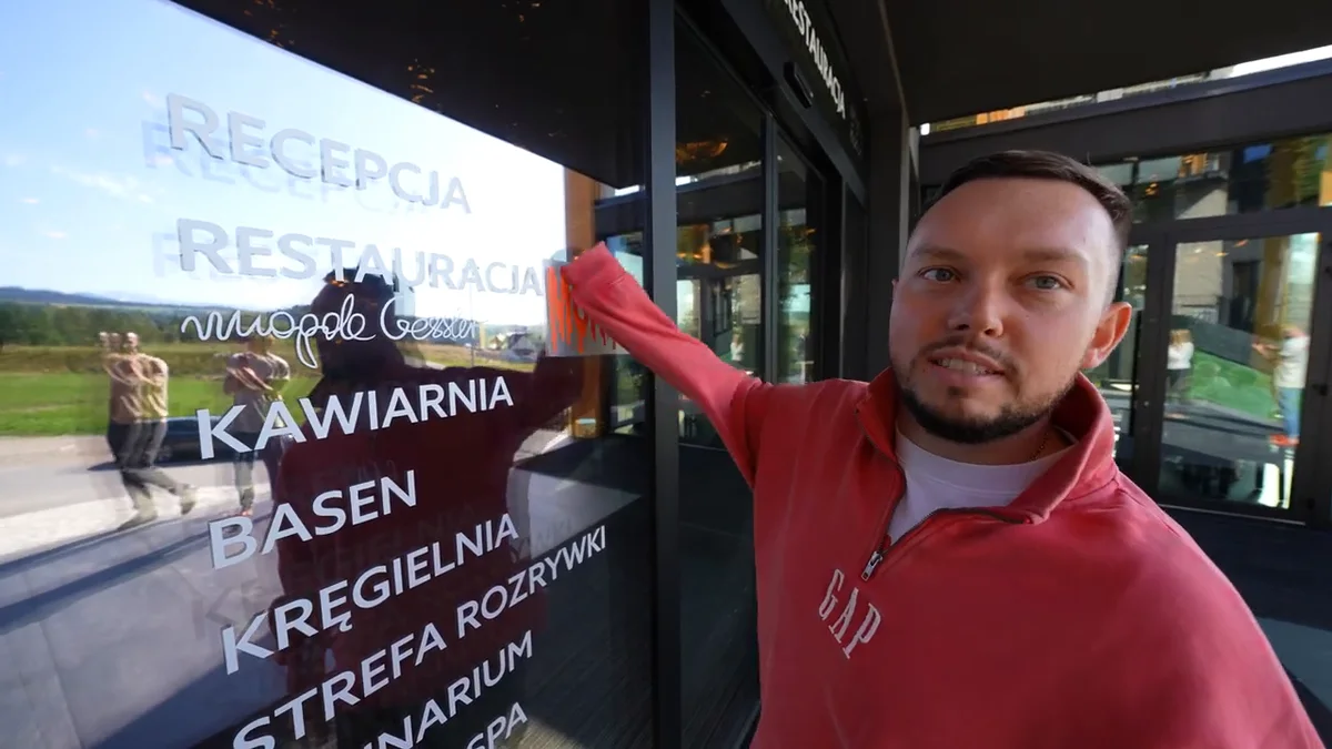 Książulo naklejający muala na szklanych drzwiach restauracji Natura obok napisów Recepcja, Restauracja i podpisu Magdy Gessler