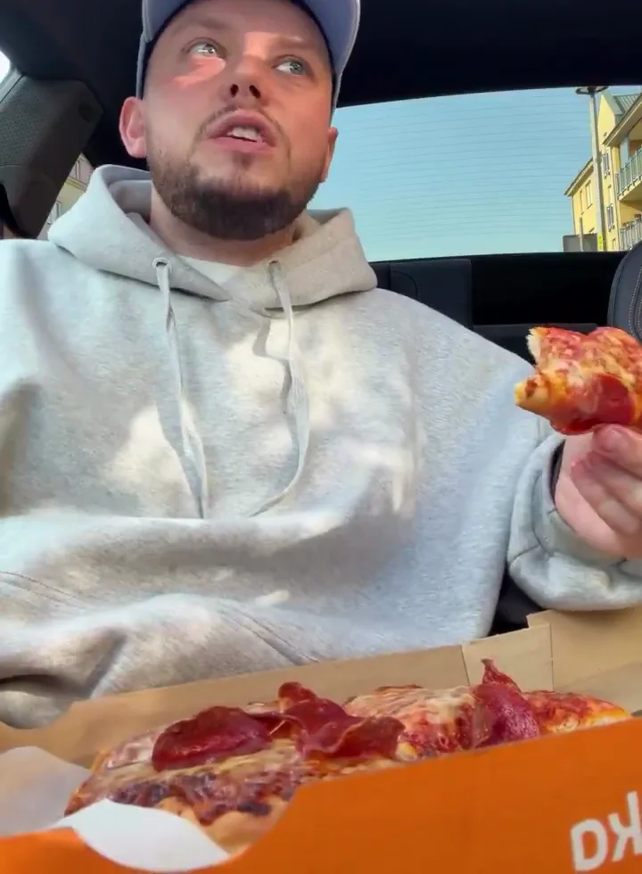 Książulo je swoją pizzę pepperoni w samochodzie, przed nim pudełko z Żabki