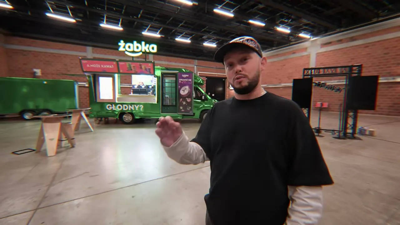 Książulo w hali przed food truckiem Żabki z napisem Głodny, przed testem pizzy z widzami