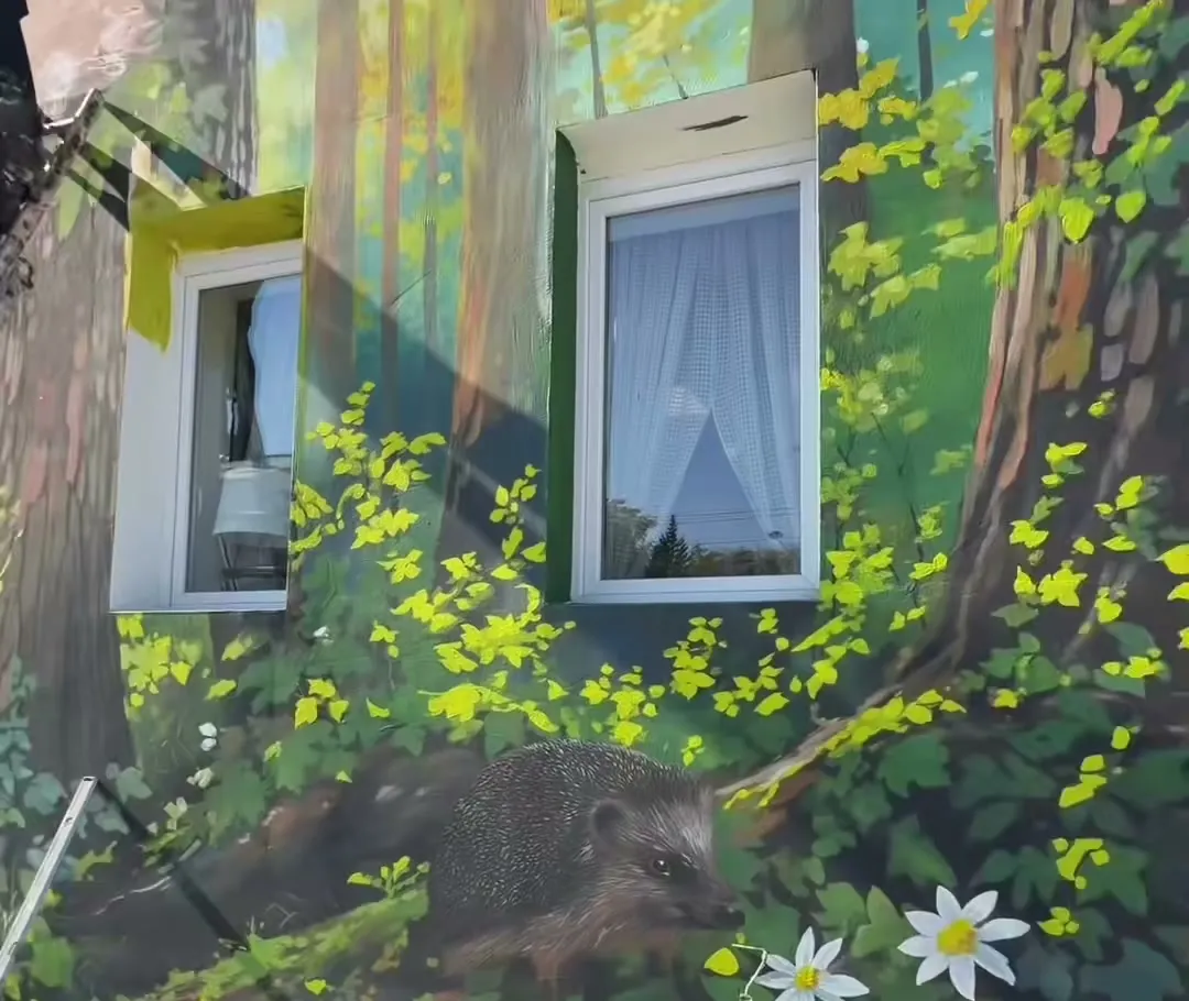 Mural na elewacji Leśnego Baru Mlecznego: jeż wśród liści i białych kwiatów, drzewa namalowane wokół okien