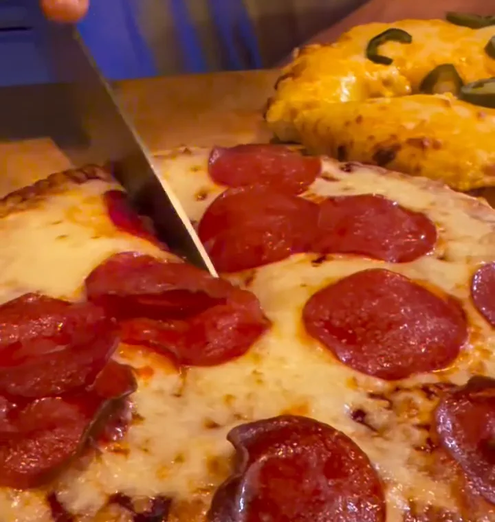 Pizza Fat Peppa krojona na desce w Polkowickiej Zapiekance, w tle Fat Cheese z jalapeño