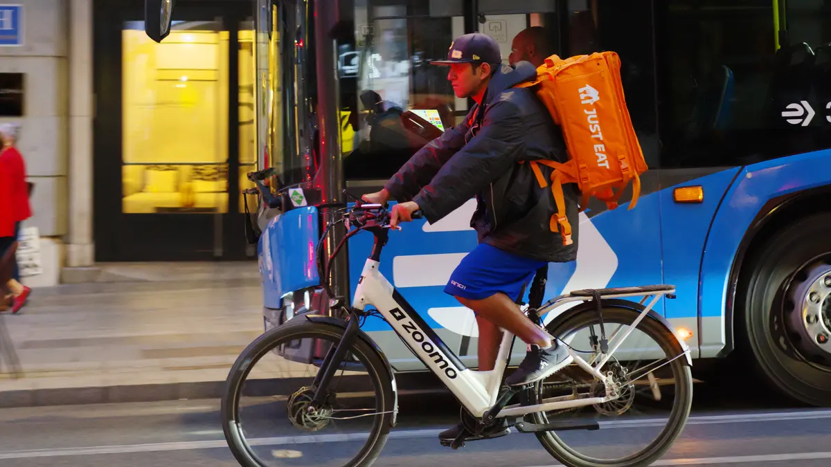 Kurier Just Eat z pomarańczową torbą na rowerze elektrycznym na ulicy w Madrycie