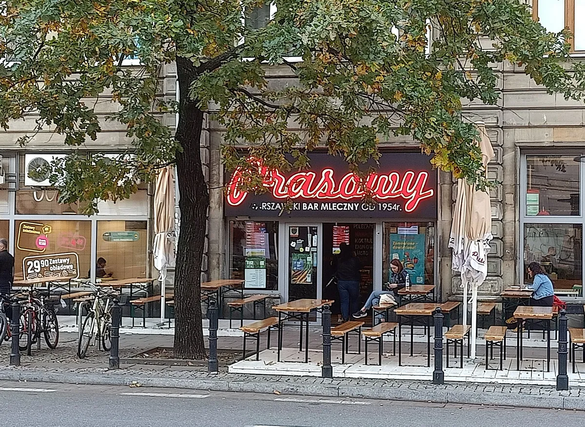 Fasada Baru Mlecznego Prasowy z czerwonym neonem i stolikami na chodniku