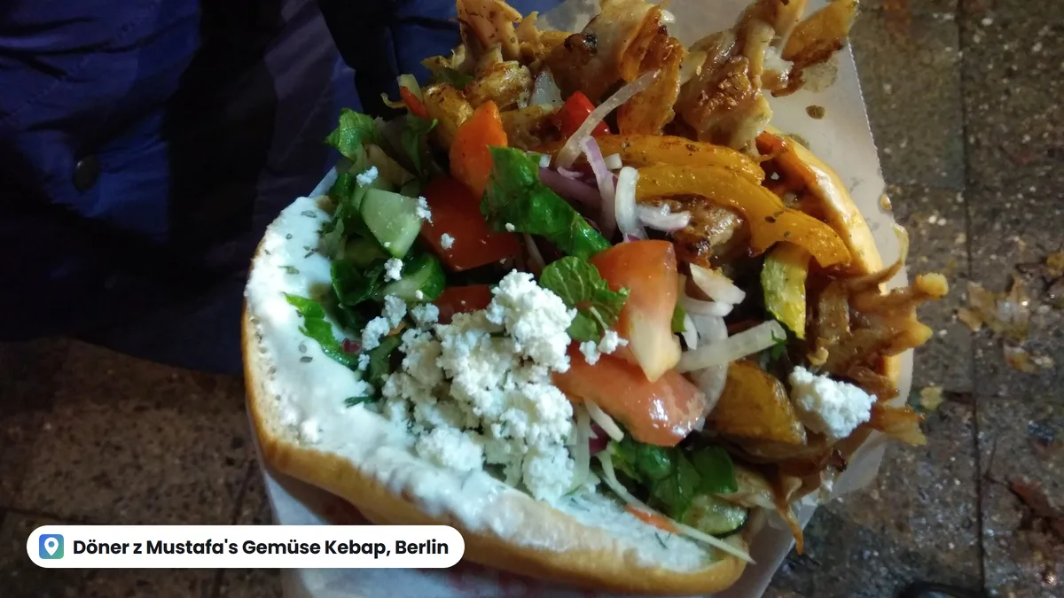 Kebab w bułce z kurczakiem, warzywami i białym serem, trzymany w papierze na ulicy